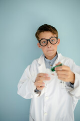 young cool boy ,with big massive black glasses is dressed up as a mad scientist holding beaker and vials in hand in front of blue background