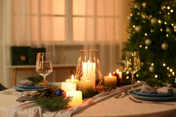 Christmas table setting with burning candles and fir branches in dining room