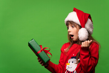 Emotional girl in a knitted sweater and Santa's hat looks in surprise at a cool gift. Guess the surprise. Merry Christmas and Happy New Year 2023