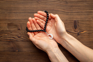 Praying hands hold black Muslim rosary with silver crescent moon