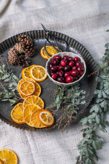 Weihnachtsdeko auf einem Teller aus Metall, eine Schale mit Cranberrys, getrocknete Orangenscheiben, Zapfen, Nüsse und Mimosenzweig, dekorieren im Advent