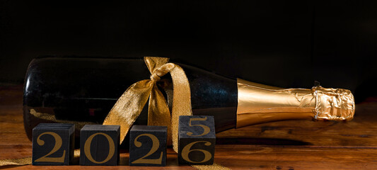 New Year 2025 / 2026 Sylvester New Year's Eve celebration holiday greeting card banner - Black cubes with year on sparkling wine or champagne bottle on table and black background