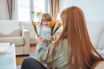 Horizontal shot of happy girl giving bunch of tulips to her mom and hugging her on Mothers Day,...