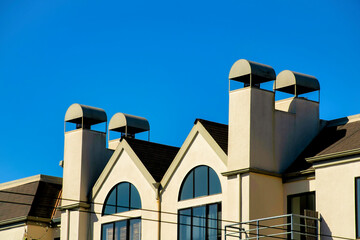 Beige stucco building with four visible chimney vents and metal tops with windows and clear blue copy space background in sun