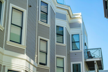 Building facade with wooden pannels and white accent paint around visible winows with clear blue sky background in late day shade