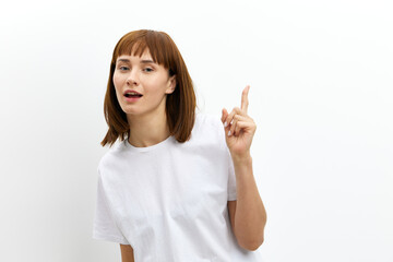 a pleasant, beautiful, attractive woman stands on a white background in a white T-shirt and looking at the camera shows her index finger up