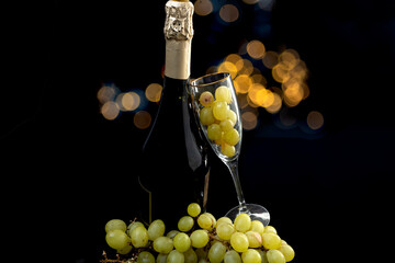 Cava or champagne bottle with glass and grapes on a black background with bokeh lights, for New Year's Eve
