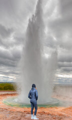A young woman in sporty clothes watches Eruption of Strokkur Geyser in Haukadalur Valley - 
 Iceland