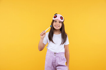  Studio shot of smiling little girl in white t-shirt and eye mask holding  toothbrush looking to...