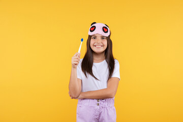  Studio shot of smiling little girl in white t-shirt and eye mask holding  toothbrush looking to...