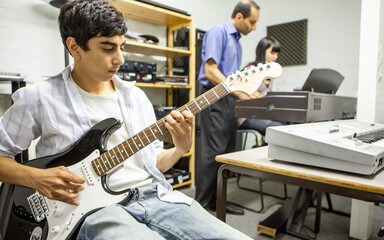 Music Students: Playing Together. A young guitarist practicing chords while teacher helps his...