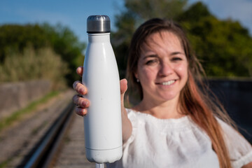 Mujer sonriente mostrando botella metálica en blanco, para anuncios o propagandas. Fotografía con...