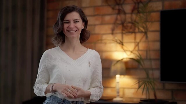 A cheerful smiling young woman, looking into the camera, make a gesture with her hands to demonstrate something or invites us to take part in something. An offer to enter into a social relationship.