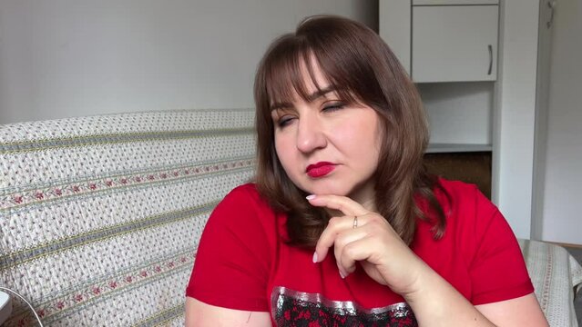 a serious and thoughtful woman 40 years old in a red T-shirt leaned on her arm looked into the camera and turned her head to the other side