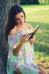 Beautiful young woman sitting in the park and reading book on a sunny summer day