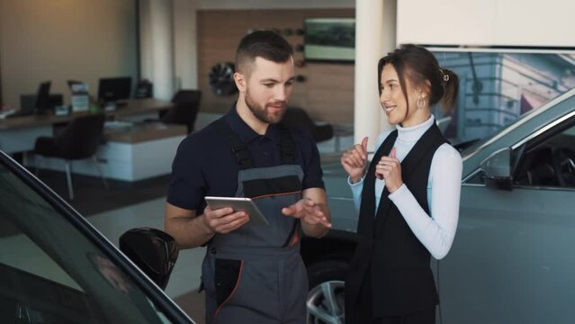 Young beautiful woman signing in tablet and thanking man in auto mechanic uniform