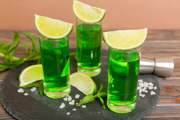Sweet refreshing mint liqueur, with ice and mint leaves on table background, Shots with lime slice and mint flat lay