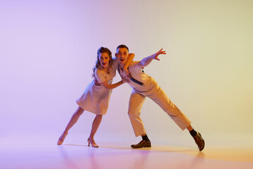 Incendiary dance. Emotional couple of dancers in retro style outfits dancing social dances isolated on gradient lilac color background in neon light. Concept of art, 60s, 70s culture