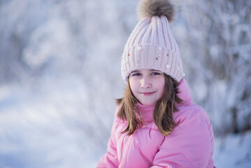 Portrait of a little happy girl in a pink hat and jacket in winter on a walk in the park, winter outdoor activities, a girl in winter clothes