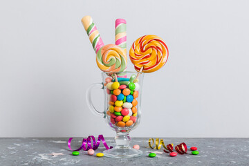 Colorful candies in cup on table on light background background. Large swirled lollipops. Creative concept of a jar full of delicious sweets from the candy store