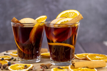 Mulled wine in transparent glass mugs cups placed on wooden table, decorated with dried fruit, red wine flavored with cinnamon sticks, spice and orange fruit