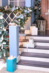 Festive outdoor design home with Xmas tree and gifts in yard. House entrance staircase decorated for winters holidays, gifts, branches fir and glowing garland. Cozy wooden porch of the house with gift