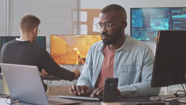 Multiethnic team of video game developers working on creation of fps game in contemporary office, sitting by computers at their workplaces