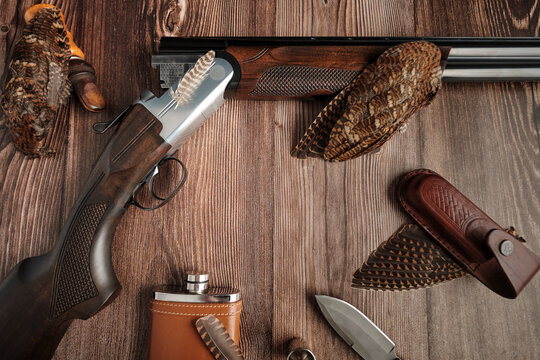 hunting stories: a double-barreled shotgun, a hunting knife, a flask for liquor, plumage of a woodcock on a wooden tabletop background, copy space