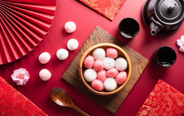 Obraz na płótnie Canvas Tang Yuan(sweet dumplings balls), a traditional cuisine for Mid-autumn, Dongzhi (winter solstice ) and Chinese new year with plum flower and tea on red background.