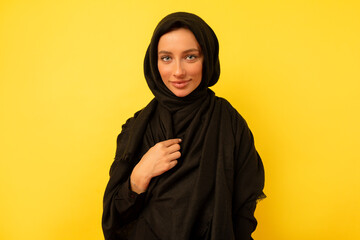 Indoor photo of eastern woman wearing black clothes looking aside with great smile on isolated yellow background