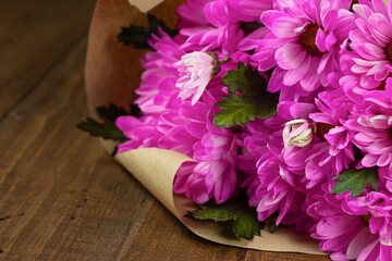 Close-up of purple chrysanthemum bouquet in craft wrapping paper on wooden table. Holiday floral composition.