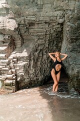 Woman swimsuit sea. Attractive blonde woman in a black swimsuit enjoying the sea air on the seashore around the rocks. Travel and vacation concept.