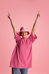 Portrait of young stylish woman with delightful expression posing in casual clothes and panama isolated over pink background