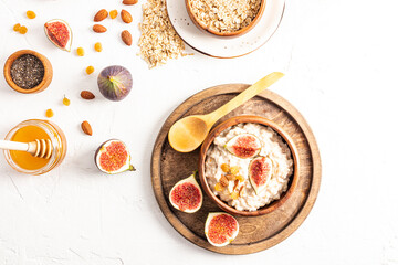 delicious healthy breakfast, oatmeal in a wooden bowl on a white table with dried fruits, figs, honey in a glass jar to improve the taste. top view.