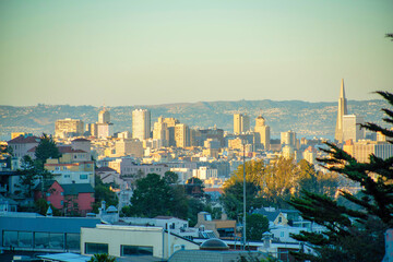 Sunlit cityscape in the background with moutains and orange and blue gradient sky with shade in city foreground late afternoon
