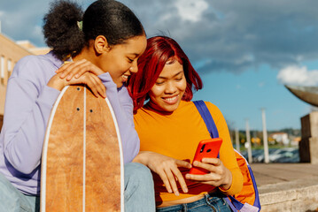 two young latin girls sitting down using the smartphone of one of them to look at applications, multimedia content and social networks. friendship concept.