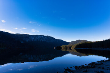 Beautiful lake in the mountains mirroring reflecting and a blue bright sky with some clouds - Eibsee, Alps