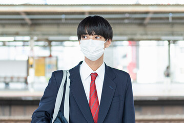 駅のホームで電車を待つ男子高校生