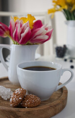A cup of coffee and a vase with tulips and daffodils on a wooden stand on a table in the kitchen