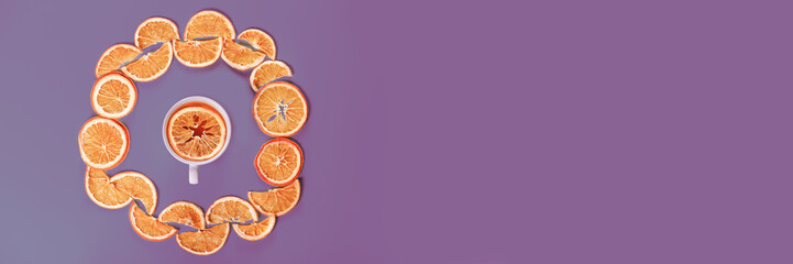 Circle of dried oranges with mug on violet background. Banner.