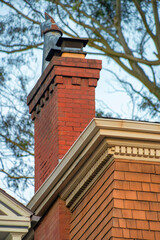 Brick chimneys with decorative yellow facade in late afternoon sunlight with visible trees in background with metal chimey vents