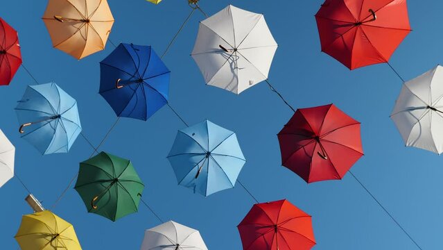 Multicolored open umbrellas in the blue sky above the city street as decoration. Smooth rotation. Background video