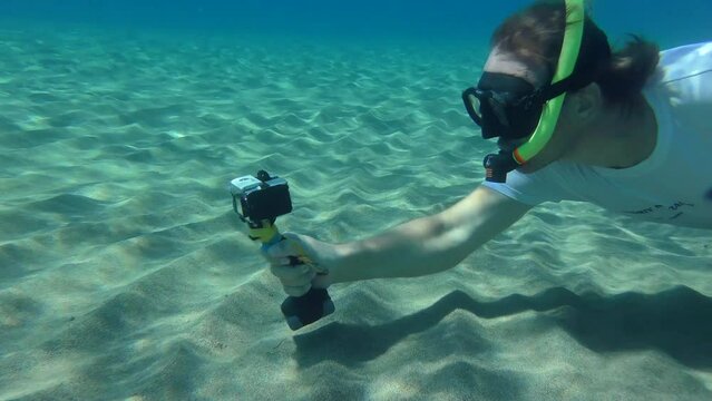 The cameraman is filming something on a sandy bottom in an underwater mask with a snorkel. Mediterranean, Greece.