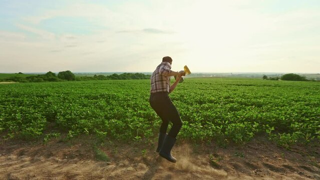 Back view of male farmer working on field, dancing, jumping. Happy, glad farmer taking care of plants, sprouts, holding spade, working in countryside. Concept of agriculture.