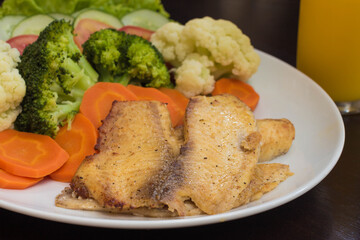 plate of vegetables served with a juicy grilled fish fillet with carrots and broccoli in the background blurred glass of orange juice