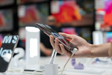 Close-up view shows the hand of a female customer choosing a black smartphone in a mobile phone store. Difficult decision, different choice