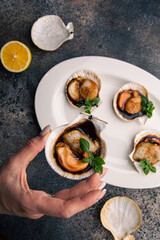 The girl holds in her hand a scallop in a sauce decorated with herbs