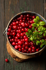 Fresh ripe lingonberry berry in a metal bowl on a wooden background, top view