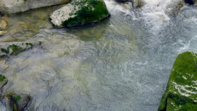 Closeup of a river flowing on mossy rocks in a field in the daylight