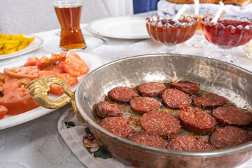 Sausage called sucuk, close up selective focus of sausage called sucuk in Turkish. Traditional frying pan in breakfast table. Hot fresh tea in glass. Tomatoes an jam blurred in background.